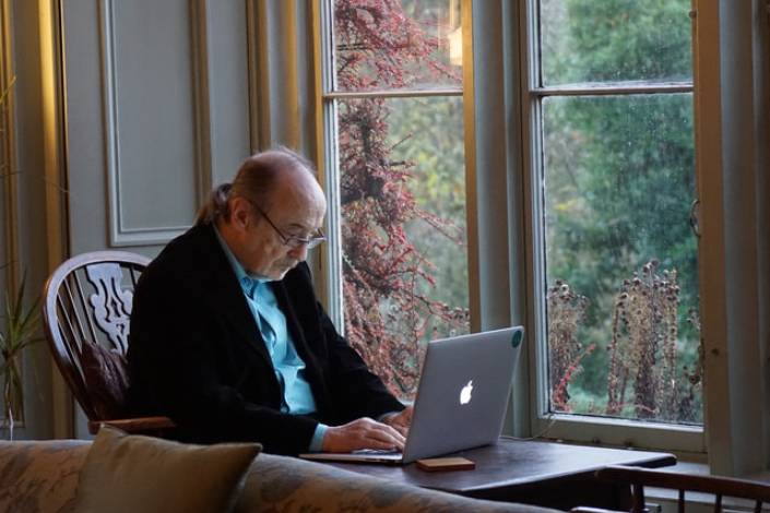 man with glasses typing on laptop next to window